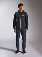 Alpinestars Transverse Hoodie, lässiger Kapuzenfleece mit Front-Reißverschluss, Schwarz, weißes Astars-Logo auf der Brust und „One Goal“-Aufdruck auf der Vorderseite, Kapuze mit Kordelzug, kombiniert mit dunkler Jeans und schwarzen Sneakern, Lifestyle-Motorsport-Streetwear