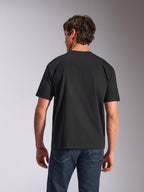 Alpinestars Aplomb Oversized CSF Tee, kurzärmeliges T-Shirt, Schwarz, Rückansicht, getragen von einem Model mit blauen Jeans, lockere Passform, lässige Sportbekleidung