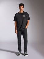 Alpinestars Wild Oversized CSF Tee, Short Sleeve T-Shirt, Black, worn by a model with black trousers and sneakers, featuring a white Astars logo and vibrant multi-color branding, casual motorsport streetwear