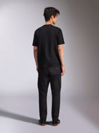 Alpinestars Noka CSF Tee, kurzärmeliges T-Shirt, Schwarz, Rückansicht eines Models, das das T-Shirt mit schwarzer Hose und Sneakern trägt, lässiger Motorsport-Streetwear-Stil