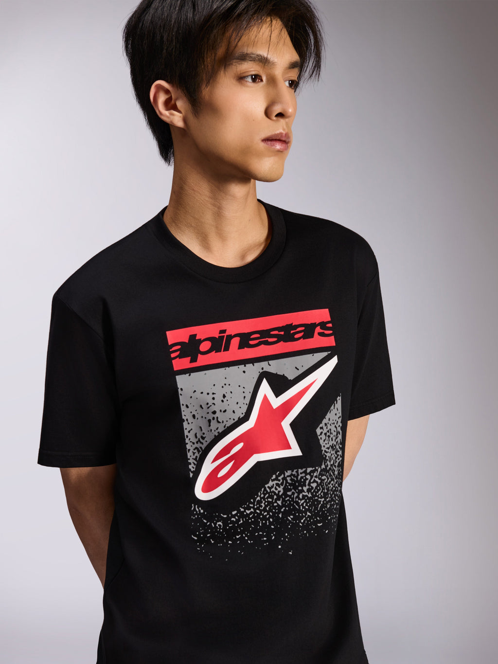 Alpinestars Noka CSF Tee, kurzärmeliges T-Shirt, Schwarz, mit rotem Branding-Block und großem rot-weißen Astars-Logo auf grau strukturiertem Hintergrund, lässige Motorsport-Streetwear