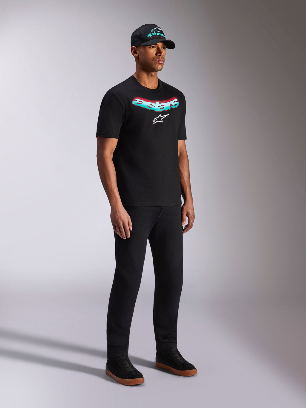 Alpinestars Ellipsoid CSF Tee, schwarzes Kurzarm-T-Shirt, Astars-Grafik mit Farbverlauf in Blaugrün und Rot und weißem Logo, männliches Model in lässiger Streetwear mit schwarzer Kappe und Hose