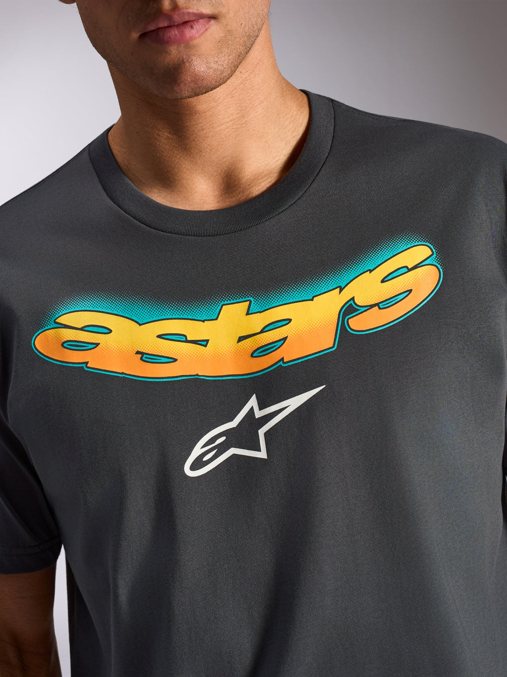 Alpinestars Ellipsoid CSF Tee, Kurzarm-T-Shirt, Anthrazitgrau, gebogener „astars“-Schriftzug mit gelb-orangefarbenem Farbverlauf und blaugrünem Punktmuster, weißes Alpinestars Stern-Logo, lässige, vom Motorsport inspirierte Bekleidung