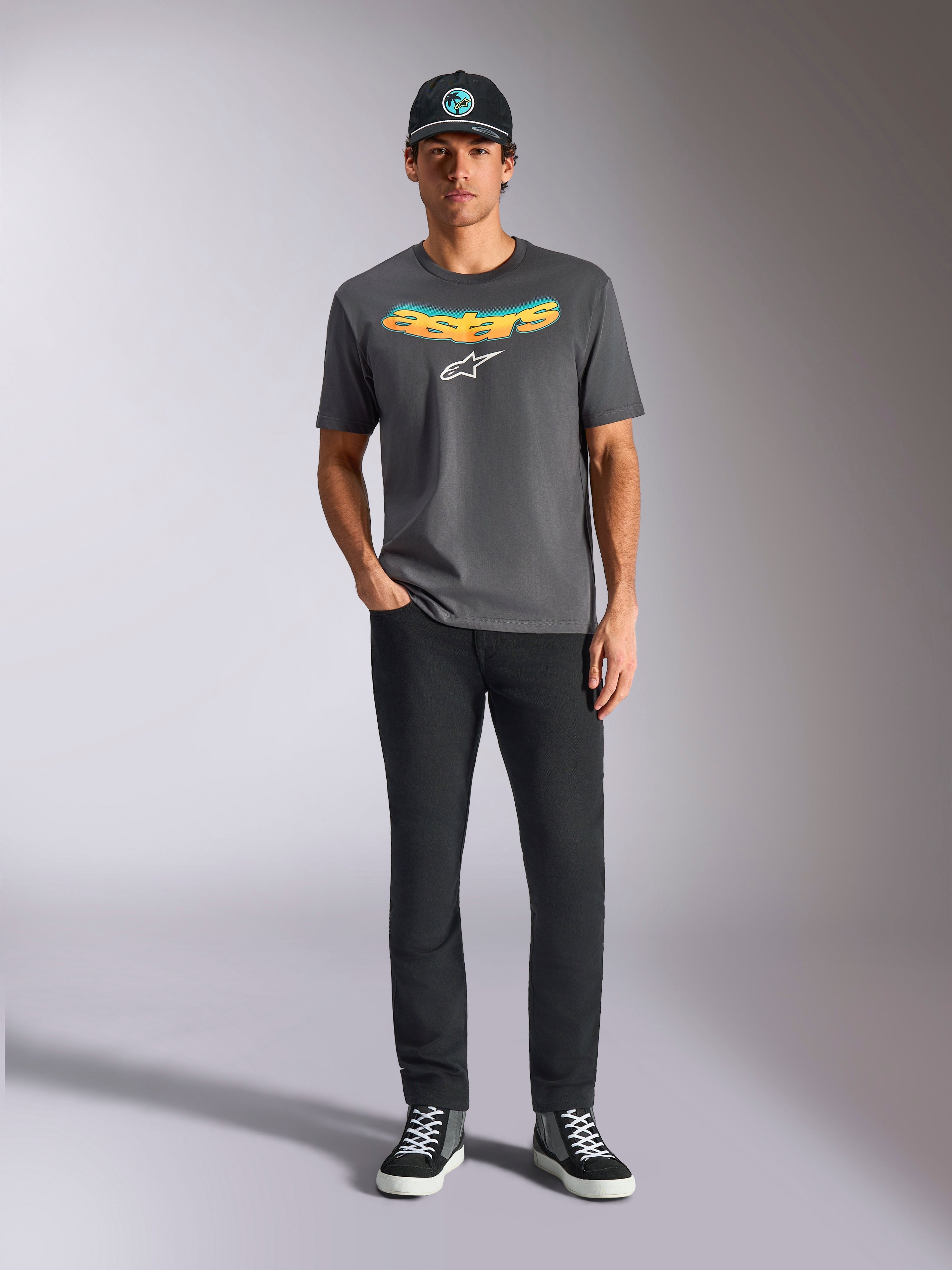 Alpinestars Ellipsoid CSF Tee, Kurzarm-T-Shirt, Anthrazitgrau, mit einem geschwungenen gelb-orangen Farbverlauf-Schriftzug und weißem Astars-Logo, getragen von einem Model mit schwarzer Hose und Baseballkappe, lässiger Sportbekleidungsstil