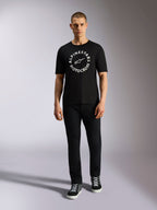 Alpinestars MX CSF Tee, Kurzarm-T-Shirt, Schwarz, weiße kreisförmige Alpinestars Motocross-Grafik, getragen von einem Model mit schwarzer Hose und Sneakern, lässige Motorsport-Streetwear