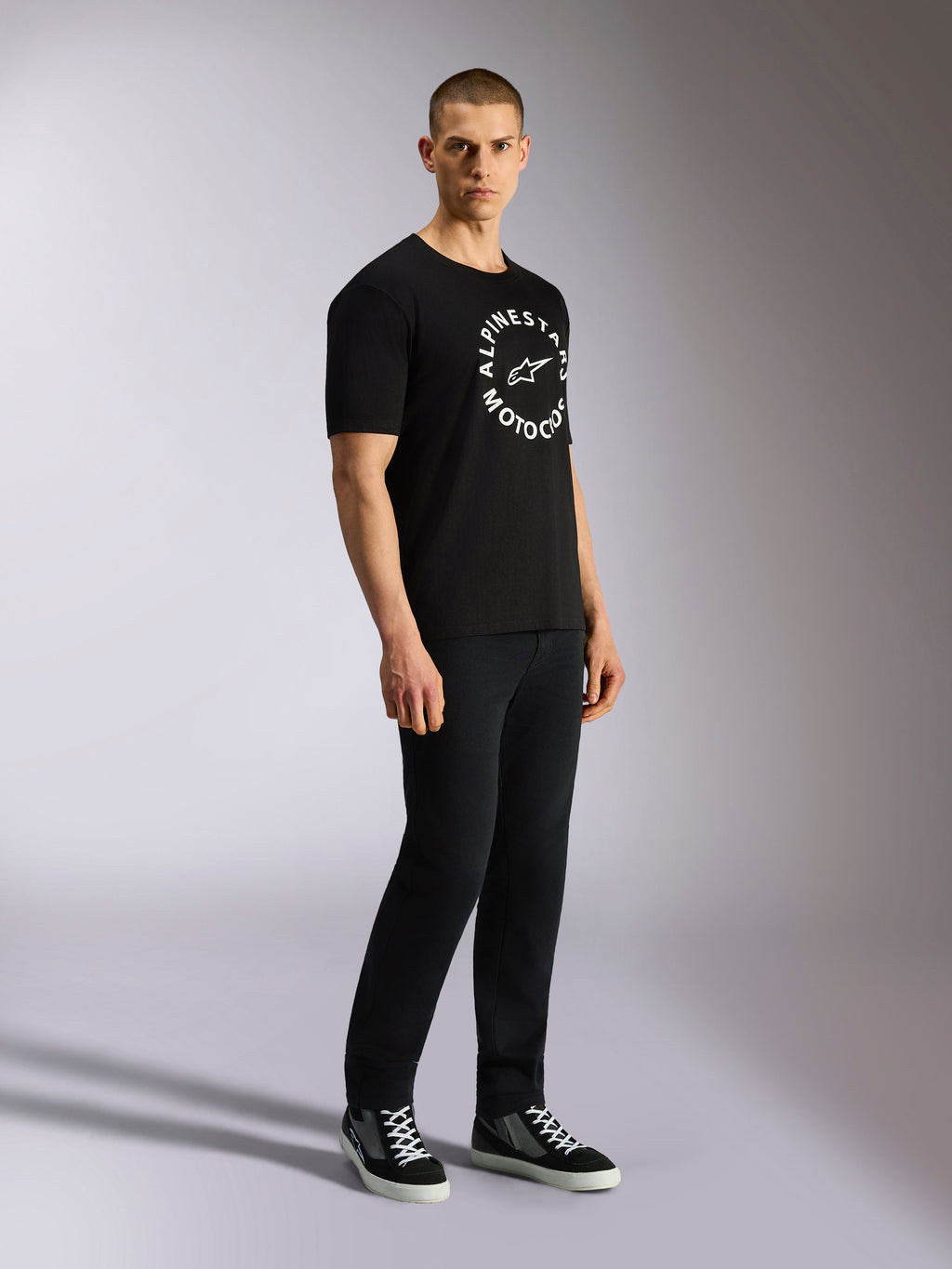 Alpinestars MX CSF Tee, Kurzarm-T-Shirt, Schwarz, weiße kreisförmige Alpinestars Motocross-Grafik auf der Brust, von einem Model mit schwarzer Hose und Sneakern getragen, lässige Motorsport-Streetwear