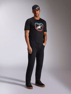 Alpinestars Plate CSF Tee, Kurzarm-T-Shirt, Schwarz, bunte MX-Plattengrafik auf der Vorderseite mit Stern-Logo, getragen von einem Model mit schwarzer Logo-Kappe und Hose, lässige, vom Motorsport inspirierte Streetwear
