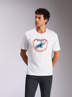 Alpinestars Plate CSF Tee, Kurzarm-T-Shirt, Weiß, mit einer Astars MX Plattengrafik auf der Vorderseite, blauem Logo und orangefarbenem Rand, getragen von einem Model, lässige Motorsport-Streetwear