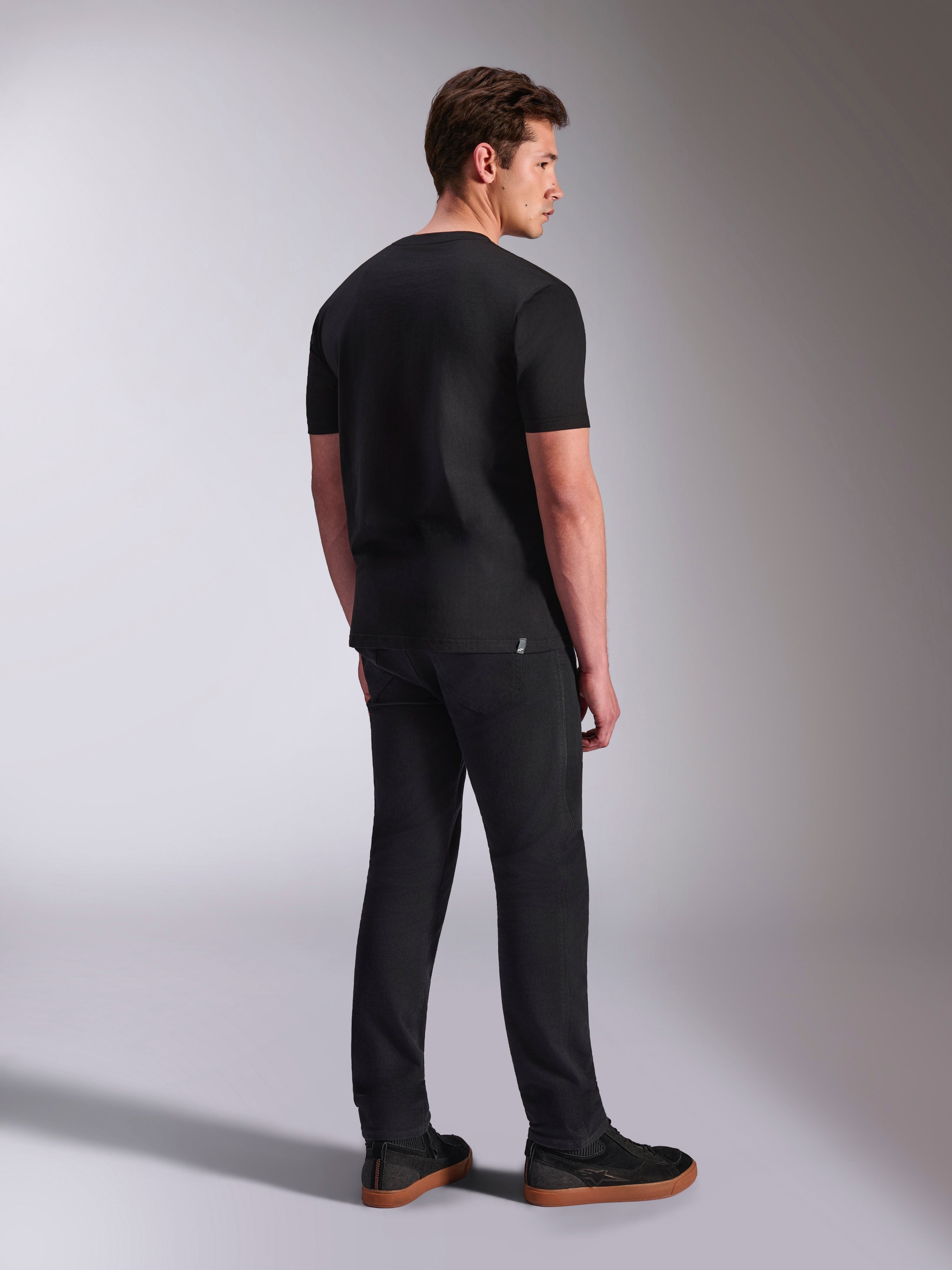 Alpinestars Abus CSF Tee, kurzärmeliges T-Shirt, Schwarz, Rückansicht an einem männlichen Model, lässige Motorsport-Streetwear, kombiniert mit dunkler Hose und Sneakern