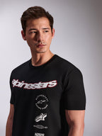 Alpinestars Abus CSF T-Shirt, kurzärmeliges T-Shirt, Schwarz, getragen von einem Model, mit weißem Alpinestars-Schriftzug mit roter Umrandung und mehreren gestapelten Grafik-Logos auf der Brust, Casual Motorsport Streetwear