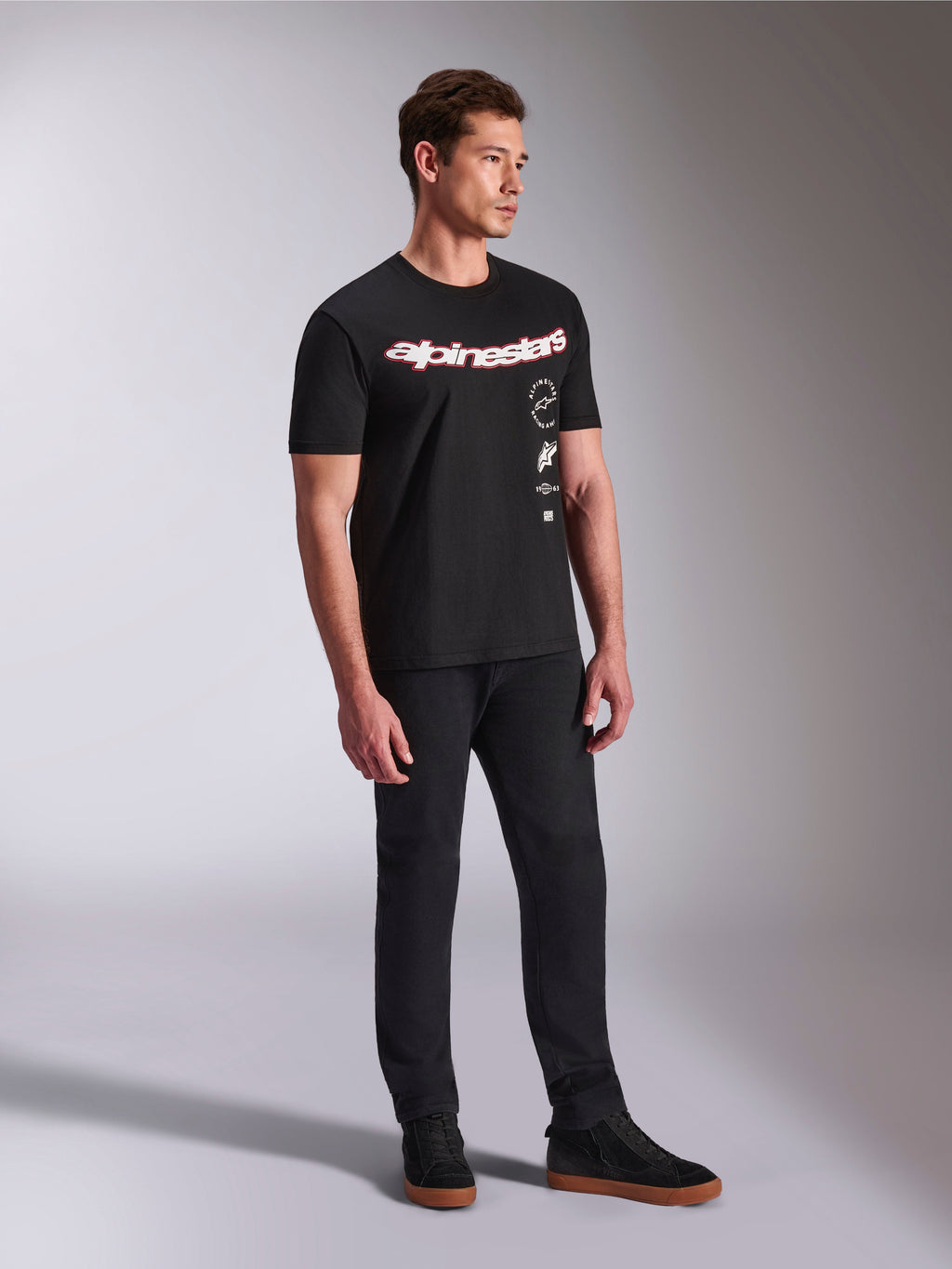 Alpinestars Abus CSF T-Shirt, kurzärmeliges T-Shirt, Schwarz, mit geschwungenem rot-weißen Alpinestars-Logo und vertikal gestapelten Grafiken, getragen mit schwarzer Hose und Sneakern, lässige motorsport-inspirierte Streetwear