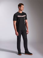 Alpinestars Abus CSF T-Shirt, kurzärmeliges T-Shirt, Schwarz, mit geschwungenem rot-weißen Alpinestars-Logo und vertikal gestapelten Grafiken, getragen mit schwarzer Hose und Sneakern, lässige motorsport-inspirierte Streetwear