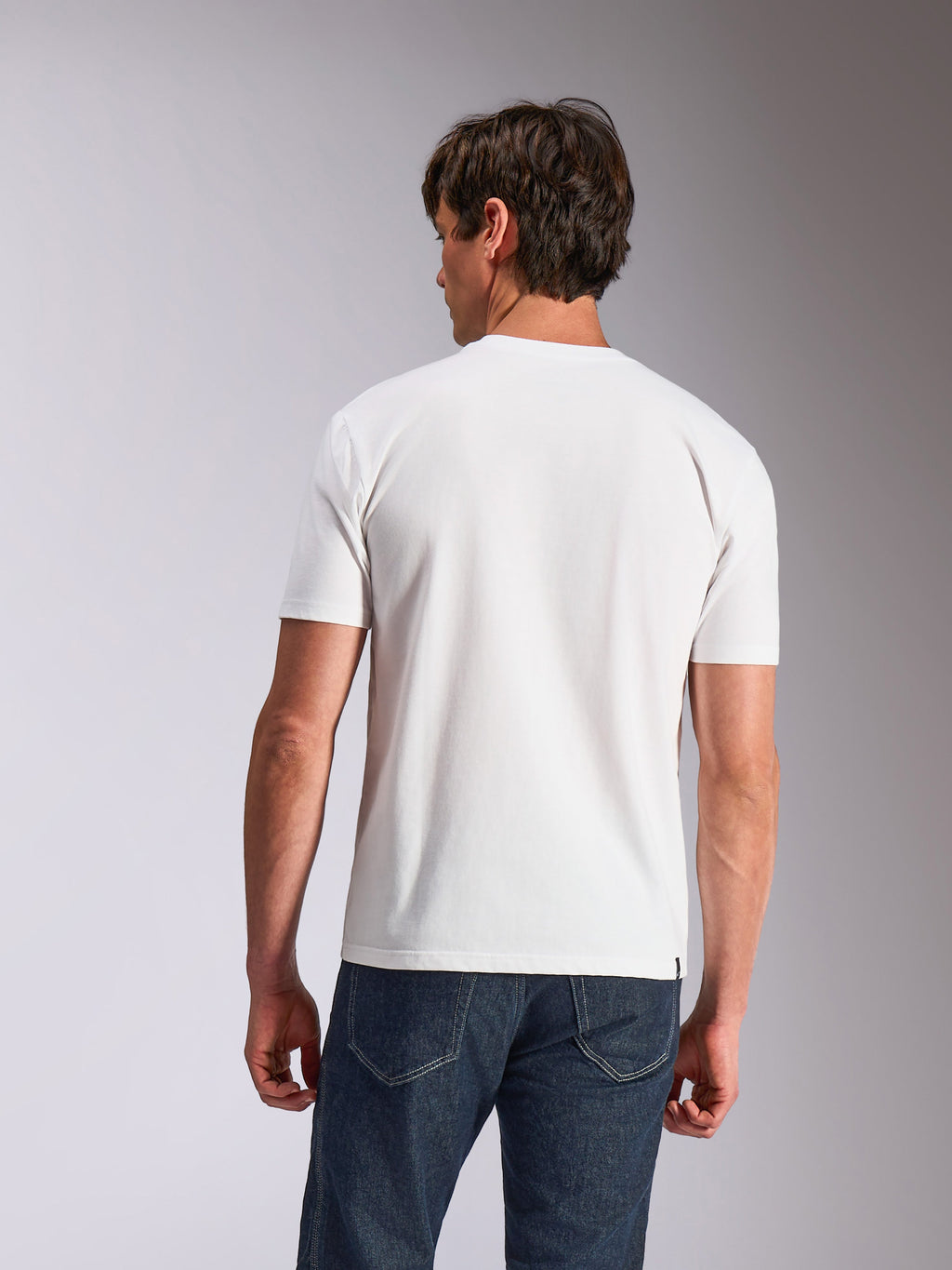 Alpinestars Abus CSF Tee, Kurzarm-T-Shirt, Weiß, Rückansicht eines Models, das ein schlichtes weißes T-Shirt und dunkelblaue Jeans trägt, lässige vom Motorsport inspirierte Lifestyle-Bekleidung