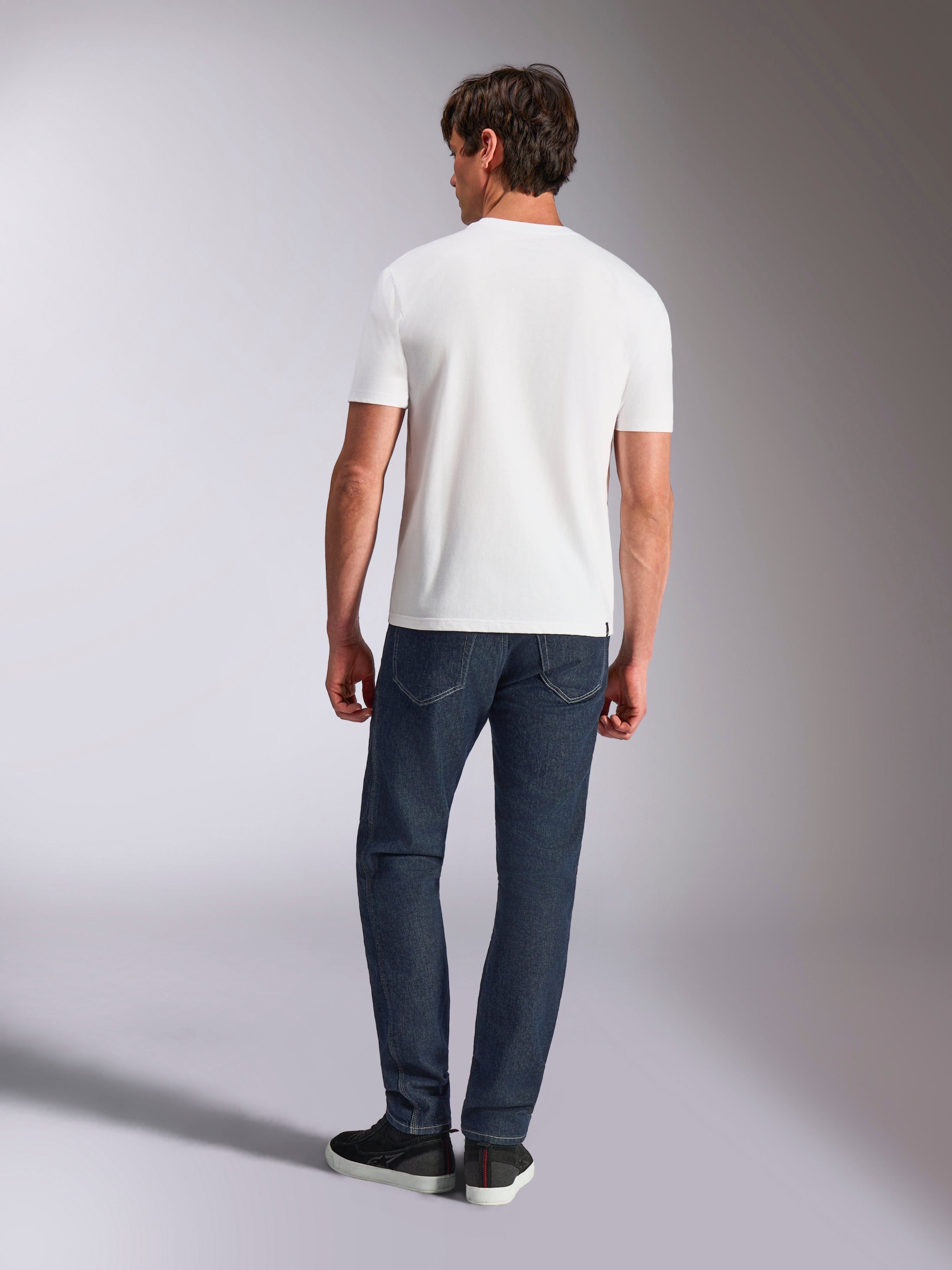 Alpinestars Abus CSF Tee, kurzärmeliges T-Shirt, Weiß, Rückansicht eines Models in weißem T-Shirt und dunkler Denim-Jeans, lässige, vom Motorsport inspirierte Streetwear