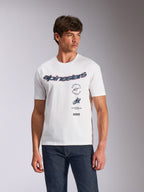 Alpinestars Abus CSF Tee, kurzärmeliges T-Shirt, Weiß, geschwungenes Alpinestars-Logo mit mehreren gestapelten Grafiken auf der Brust, getragen von einem Model mit dunklen Denim-Jeans, lässige Motorsport-Streetwear