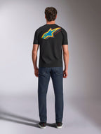 Alpinestars Angler CSF Tee, Kurzarm-T-Shirt, Schwarz, Rückansicht eines Models im Shirt mit großem, leuchtendem, mehrfarbigem Astars-Sternlogo und „RACING AHEAD“-Text, kombiniert mit dunkelblauen Jeans, lässige Motorsport-Streetwear
