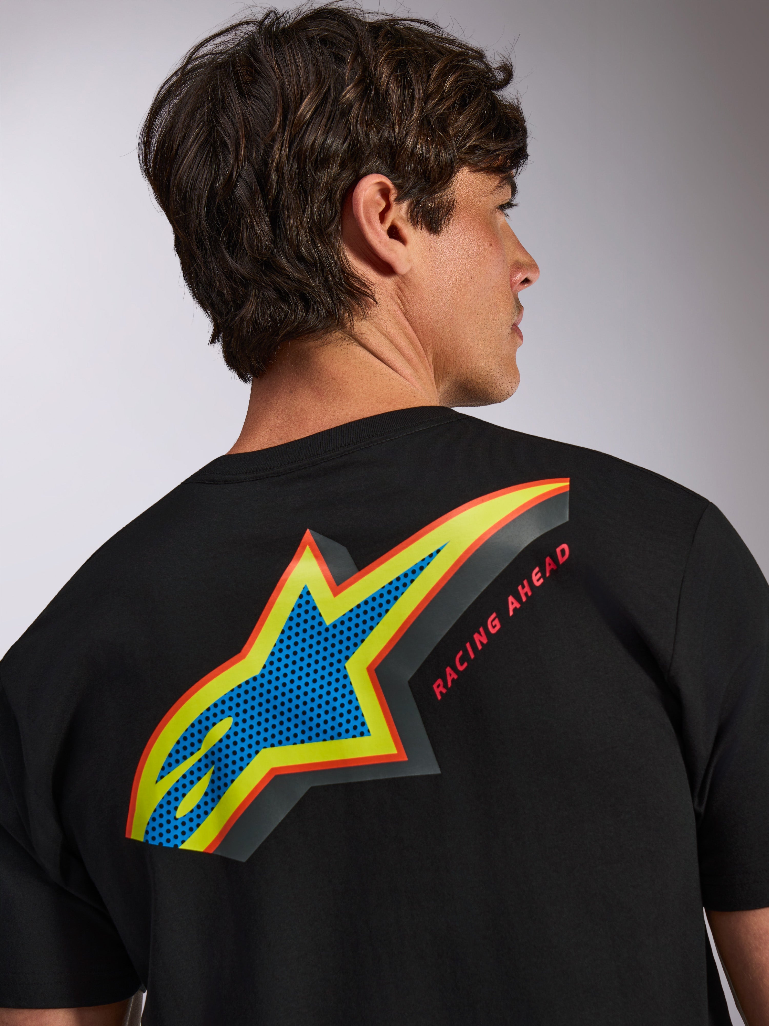 Alpinestars Angler CSF Tee, kurzärmeliges T-Shirt, Schwarz, großes mehrfarbiges Astars-Logo auf der Rückseite mit blauem, perforiertem Design, gelben und roten Umrandungen und dem Schriftzug 'RACING AHEAD', lässige Motorsport-Streetwear