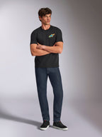 Alpinestars Angler CSF Tee, kurzärmeliges T-Shirt, Schwarz, lebendiges mehrfarbiges Astars-Logo auf der Brust, Modell mit verschränkten Armen, dunkle Denim-Jeans und schwarze Sneaker, lässige Motorsport-Streetwear