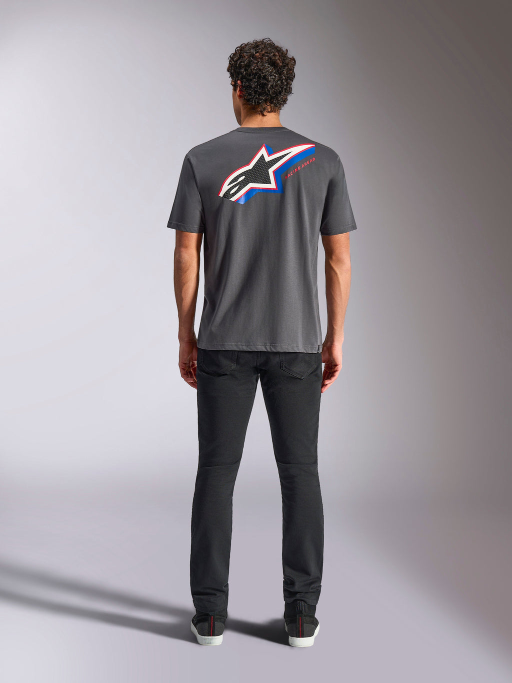 Alpinestars Angler CSF Tee, Kurzarm-T-Shirt, Charcoal, Großes mehrfarbiges Astars-Logo auf der Rückseite mit roten und blauen Akzenten, Rückansicht am Model, lässige Motorsport-Streetwear