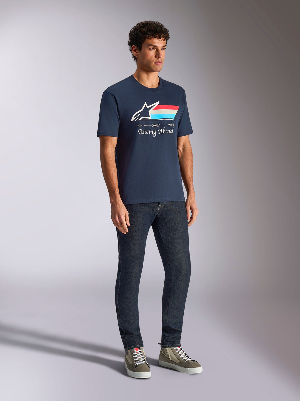 Alpinestars Trifecta CSF Tee, kurzärmeliges T-Shirt, Marineblau, mit Astars-Logo, dreifarbigen Streifen und „Racing Ahead“-Schriftzug, getragen von einem Model mit dunkler Jeans und Sneakern, lässige Motorsport-inspirierte Streetwear