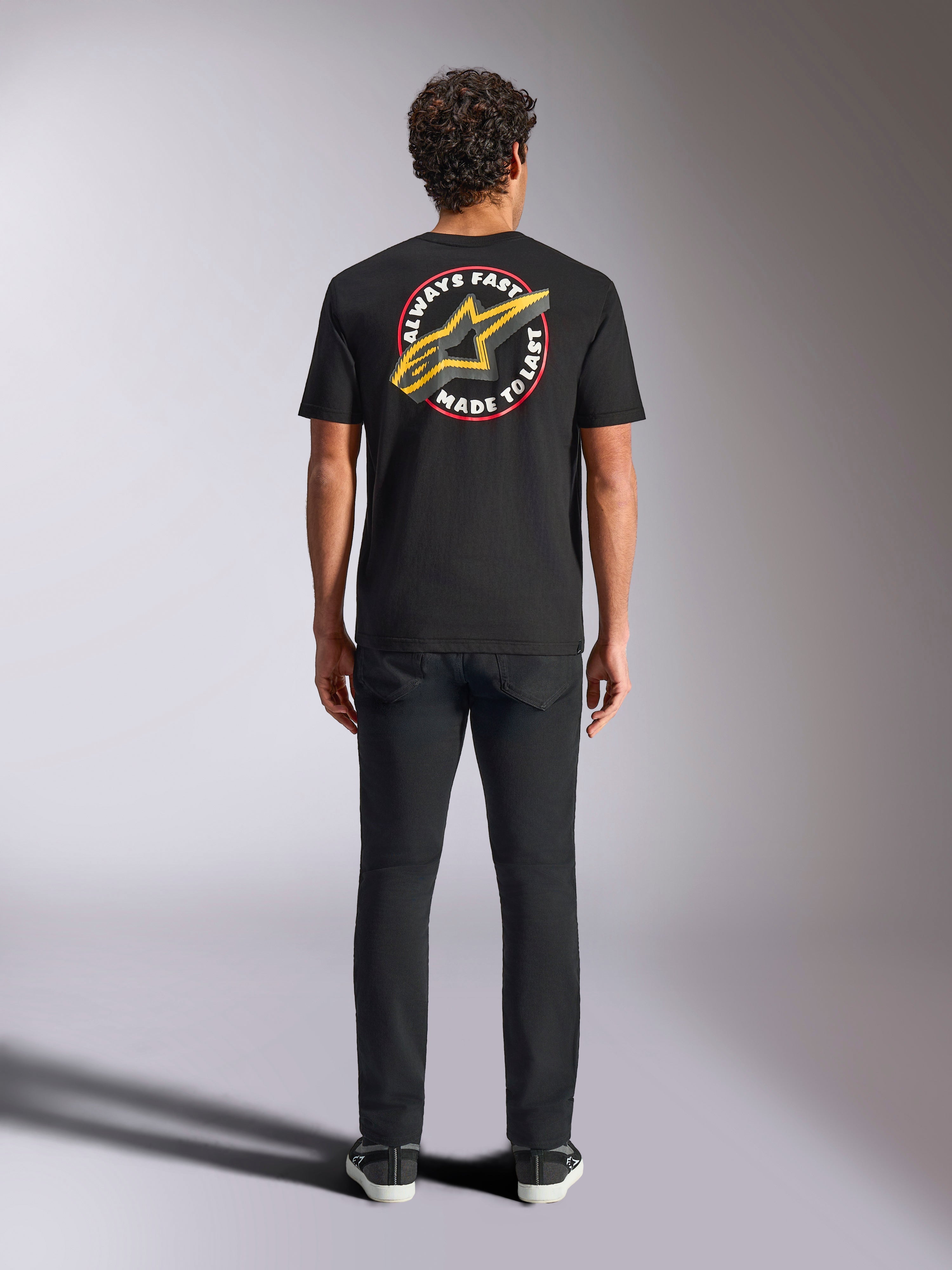 Alpinestars Aorbit CSF Tee, kurzärmeliges T-Shirt, Schwarz, Rückansicht an einem Model mit schwarzer Hose, mit großer „Always Fast Made to Last“-Grafik und gelbem Astars-Logo, lässige Motorsport-Streetwear