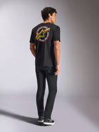 Alpinestars Aorbit CSF Tee, Kurzarm-T-Shirt, Schwarz, Rückansicht mit einem großen gelben Astars-Logo und kreisförmiger „Always Fast Made to Last“-Grafik, getragen mit schwarzen Jeans und lässigen Sneakern, Motorsport-inspirierter Streetwear-Stil
