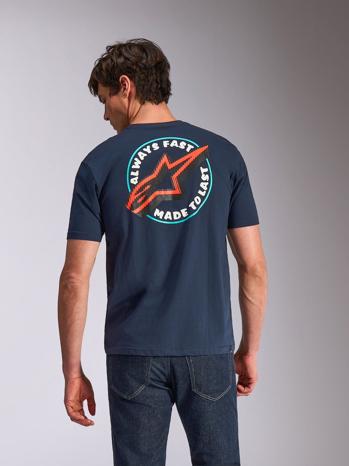 Alpinestars Aorbit CSF Tee, Kurzarm-T-Shirt, Navy-Blau, Rückansicht am Modell mit kreisförmiger „Always Fast Made to Last“-Grafik und rotem Astars-Logo, lässige motorsport-inspirierte Streetwear
