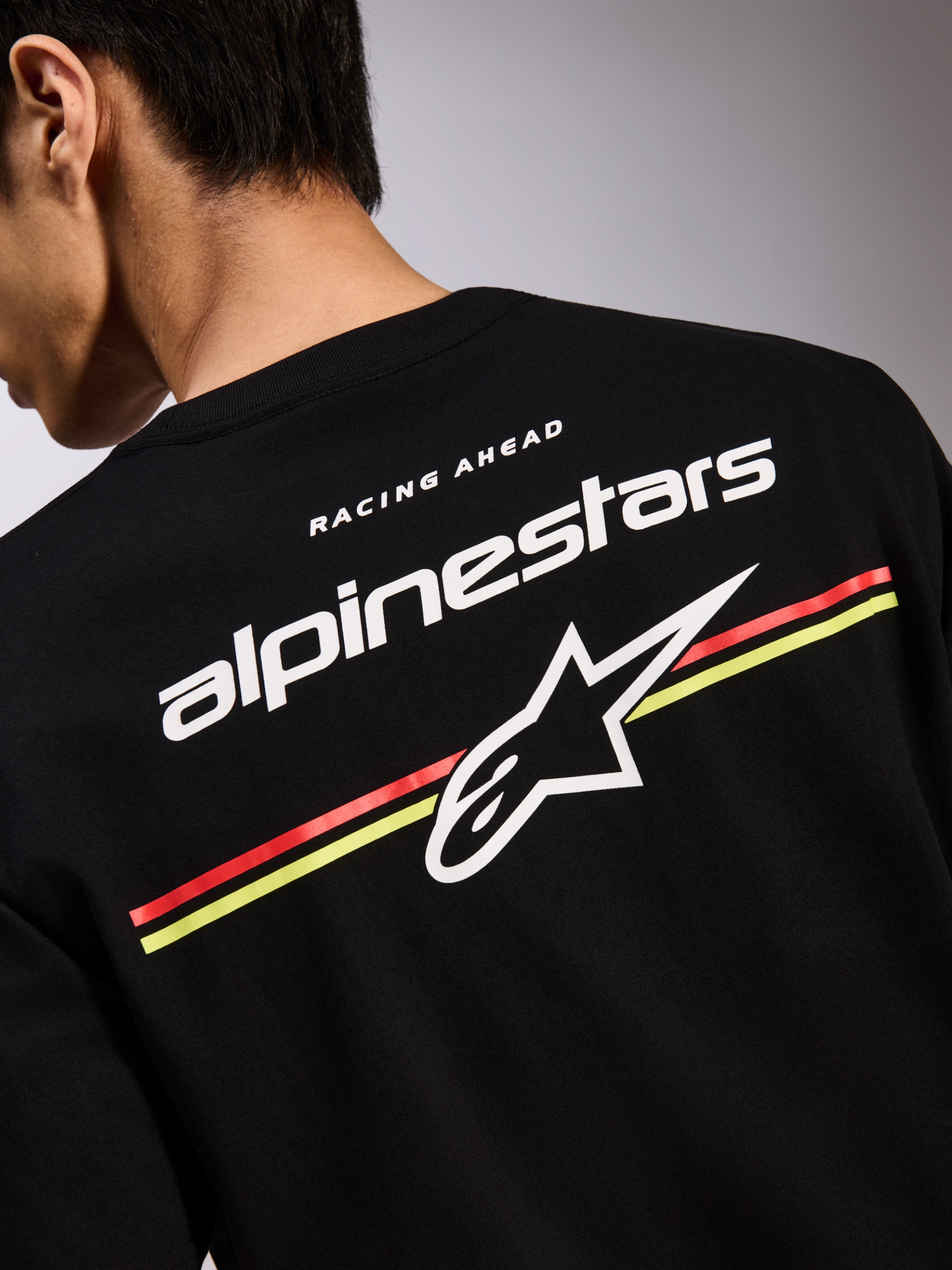 Alpinestars Lanes CSF Tee, schwarzes Kurzarm-T-Shirt, Rückengrafik mit weißen Alpinestars und Astars Logos über roten und gelben Streifen, Casual Motorsport-Streetwear