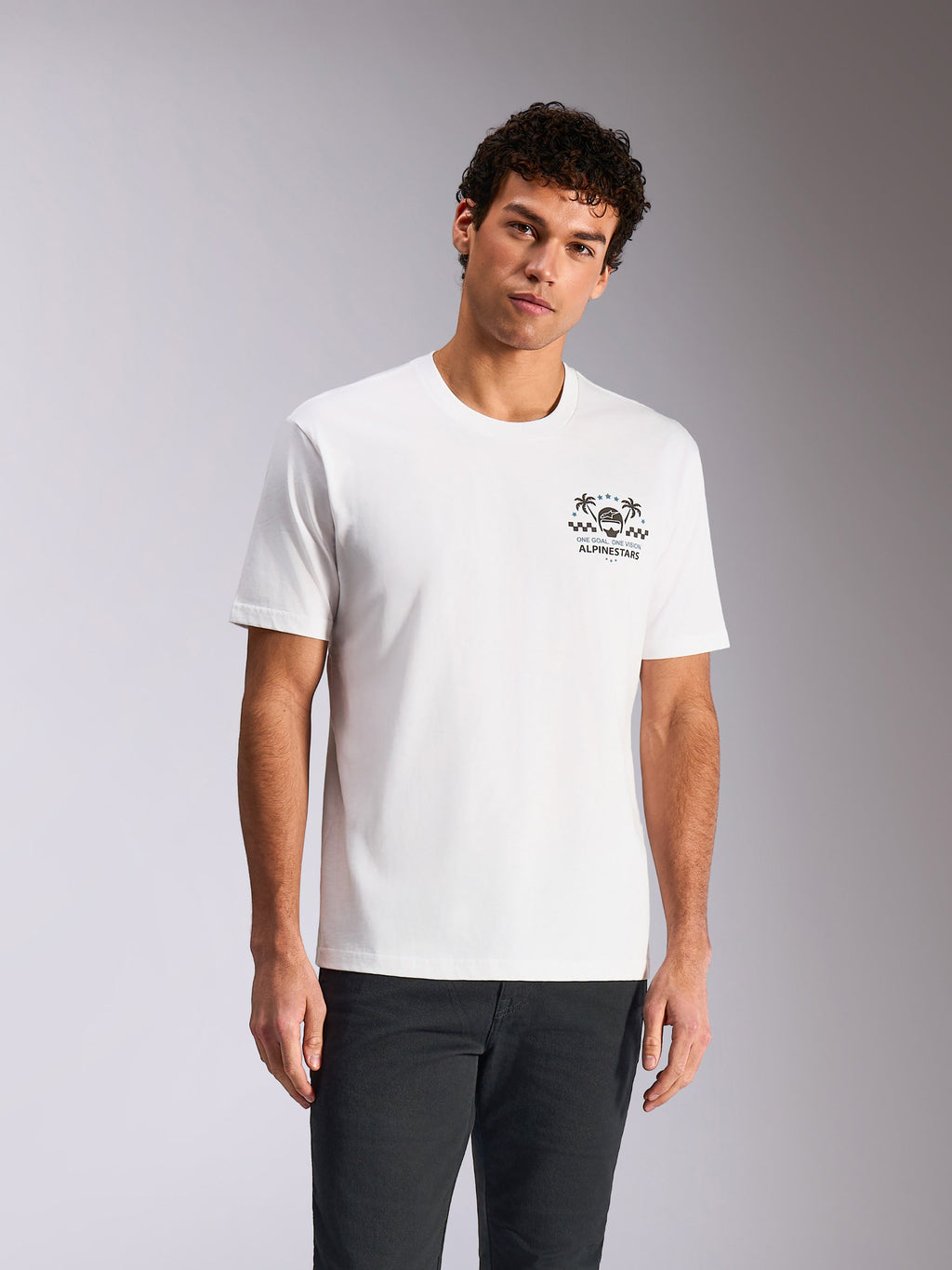Alpinestars Order CSF Tee, kurzärmeliges T-Shirt, Weiß, Brustgrafik mit Helm und Palmen, von einem Modell mit dunkler Hose getragen, lässige vom Motorsport inspirierte Streetwear
