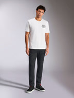 Alpinestars Order CSF Tee, Kurzarm-T-Shirt, Weiß, kleine schwarze Brustgrafik mit Helm und Palmen, lässige Motorsport-Streetwear, getragen von einem Model mit schwarzer Hose und Sneakern