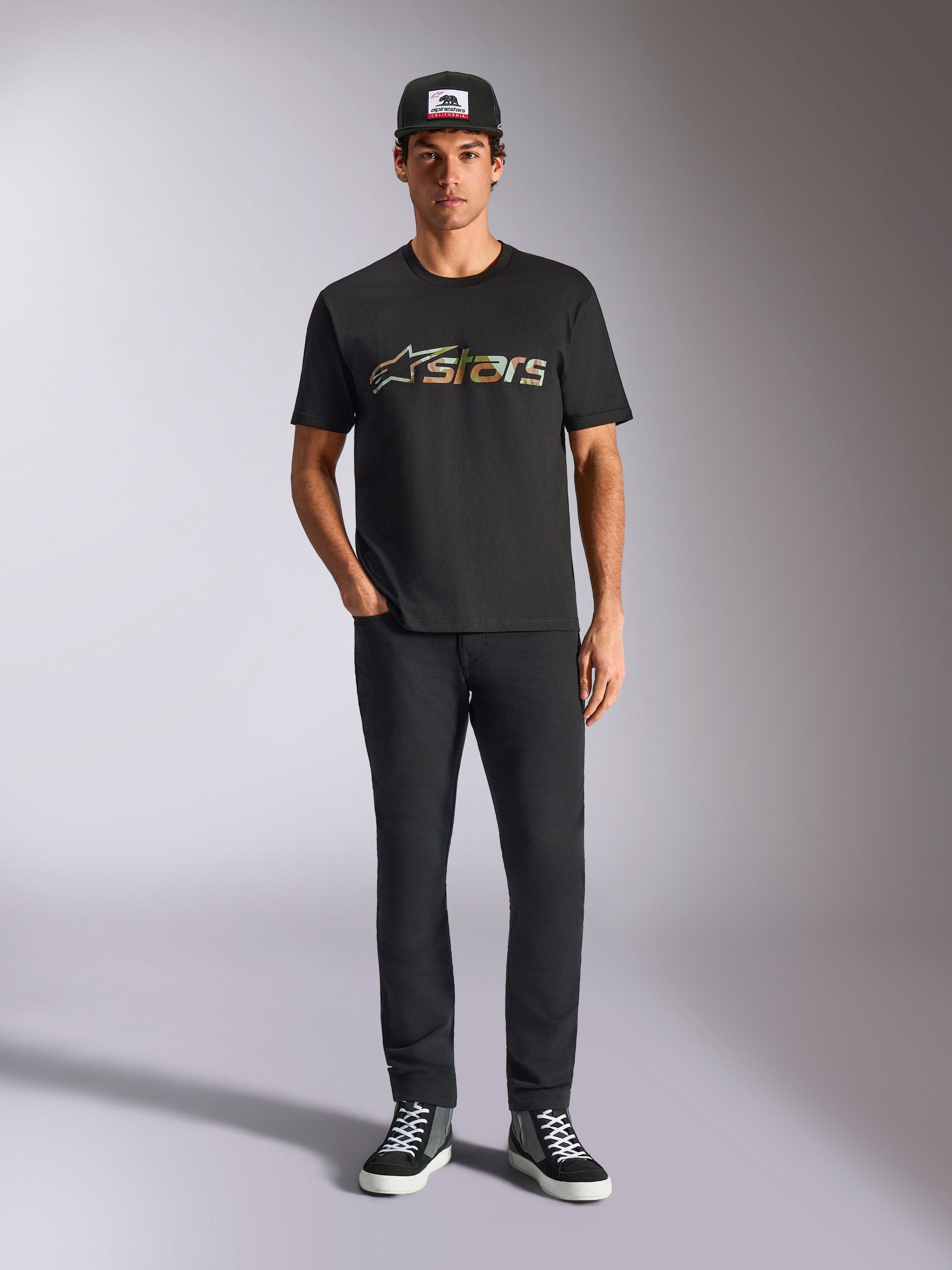 Alpinestars Verdure Camo CSF Tee, kurzärmeliges T-Shirt, Schwarz, mit einem Astars-Logo im Camouflage-Muster auf der Brust, getragen von einem Model mit schwarzer Kappe und schwarzer Hose, Casual Motorsport Streetwear