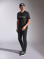 Alpinestars Verdure Camo CSF Tee, Kurzärmeliges T-Shirt, Schwarz, mit einem Astars-Logo mit Camouflage-Füllung auf der Brust, getragen von einem Model mit schwarzer Kappe und Hose, lässige Motorsport-Streetwear