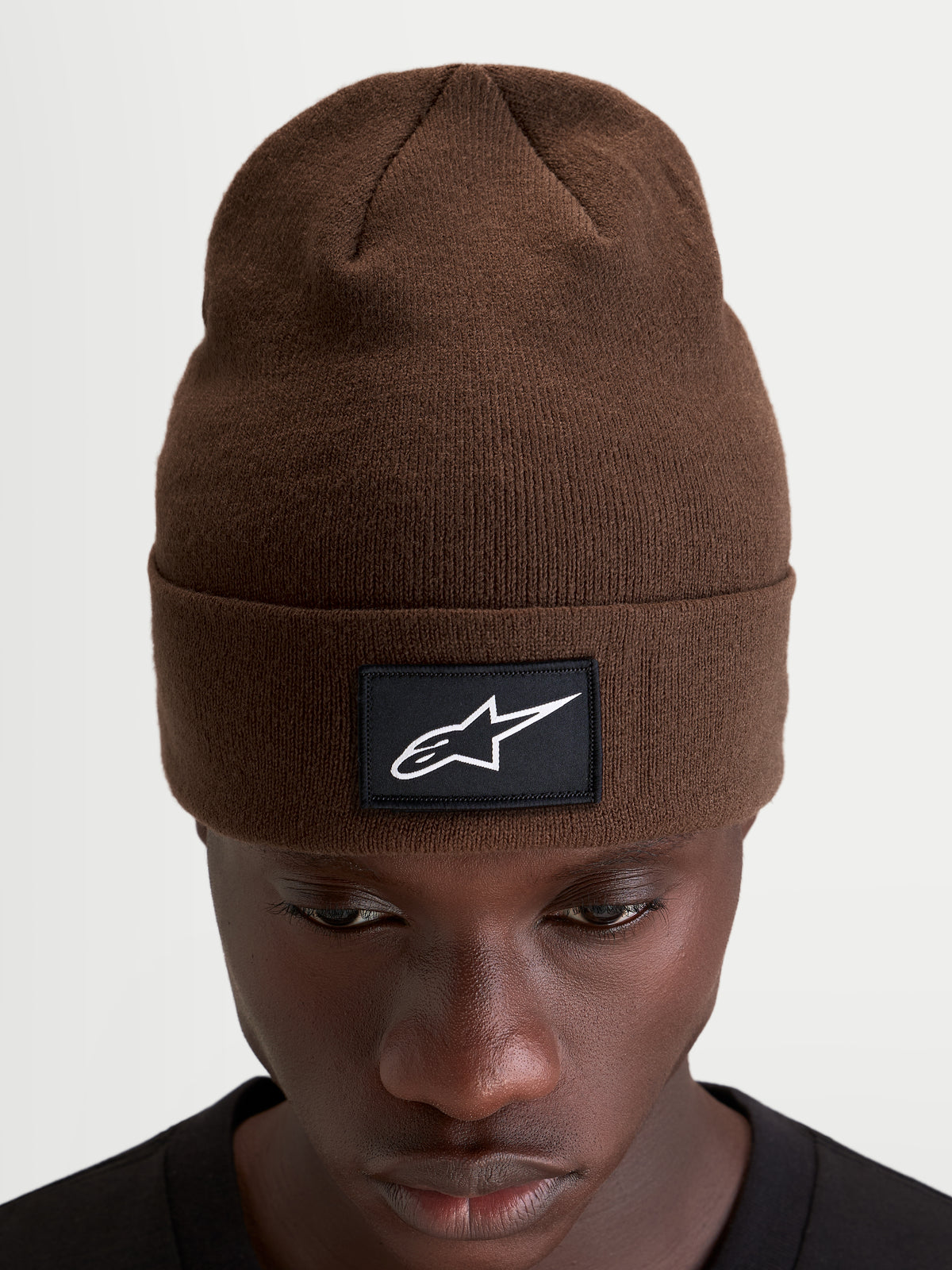Alpinestars Augment Cuff Mütze, braune Strickmütze für Sportswear, mit gewebtem schwarzem Patch und weißem Astars-Logo, getragen von einem Model in einer tiefen Passform