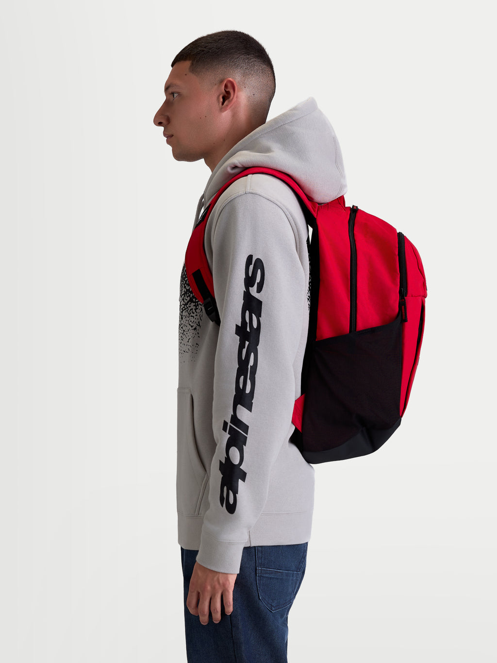Alpinestars GFX Boss Rucksack, Sportswear-Tagesrucksack, 20L Kapazität, Rot und Schwarz, robustes 600D Polyester, seitliche Netztaschen für Wasserflaschen, gepolsterte Air-Mesh-Schultergurte, am Modell gezeigt für urbanen Pendelverkehr und täglichen Gebrauch.