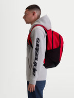 Alpinestars GFX Boss Rucksack, Sportswear-Tagesrucksack, 20L Kapazität, Rot und Schwarz, robustes 600D Polyester, seitliche Netztaschen für Wasserflaschen, gepolsterte Air-Mesh-Schultergurte, am Modell gezeigt für urbanen Pendelverkehr und täglichen Gebrauch.