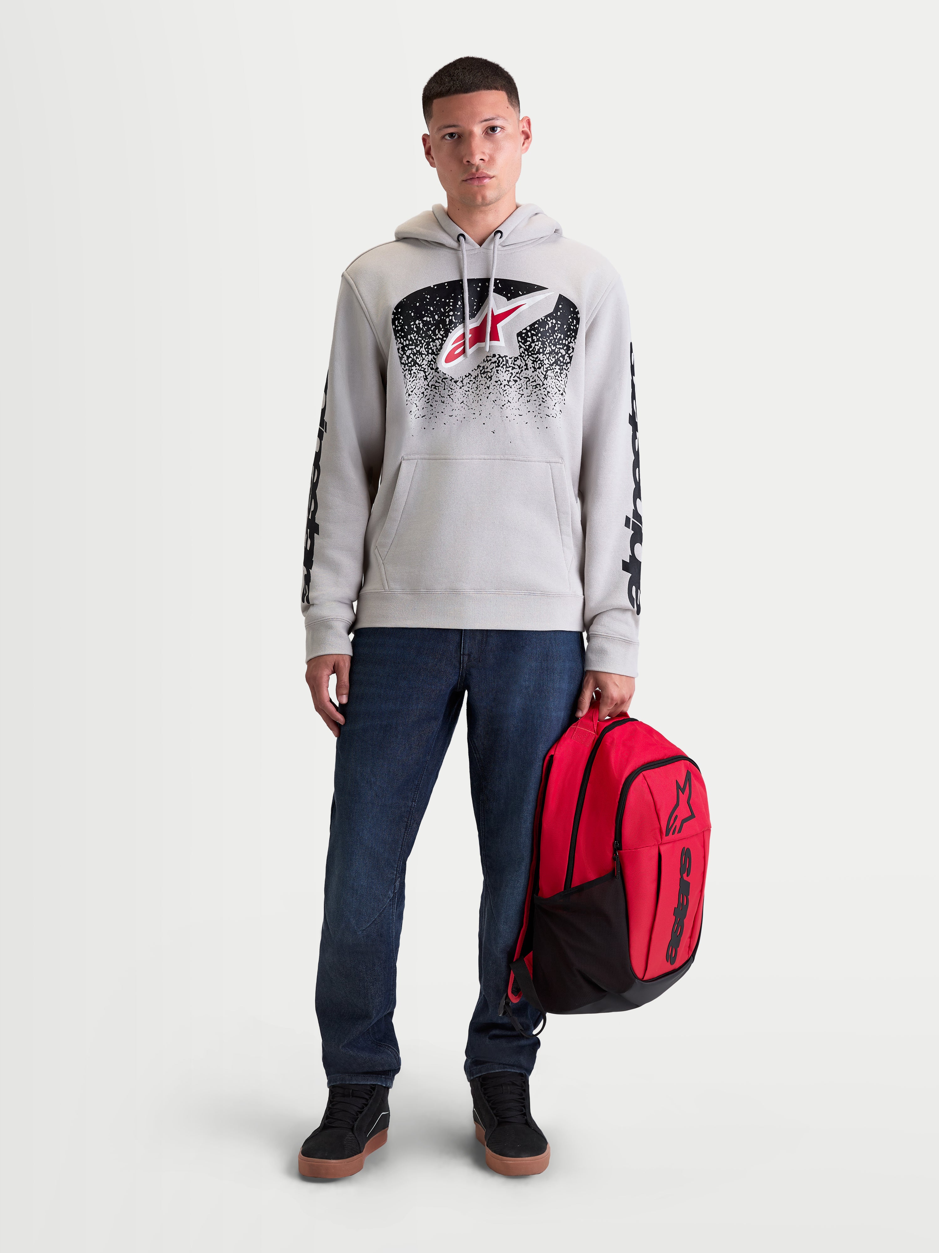 Alpinestars GFX Boss Rucksack, roter und schwarzer Sportswear-Tagesrucksack, 20L Kapazität, robuster 600D Polyester mit erhabenem Silikon-Astars-Logo, gehalten von einem männlichen Modell für den urbanen Alltag.