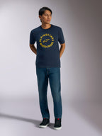 Alpinestars MX CSF Tee, kurzärmeliges T-Shirt, Navyblau, mit einer gelben kreisförmigen Alpinestars Motocross-Grafik, getragen von einem Modell mit blauen Jeans und schwarzen Sneakern, lässige Motorsport-Streetwear