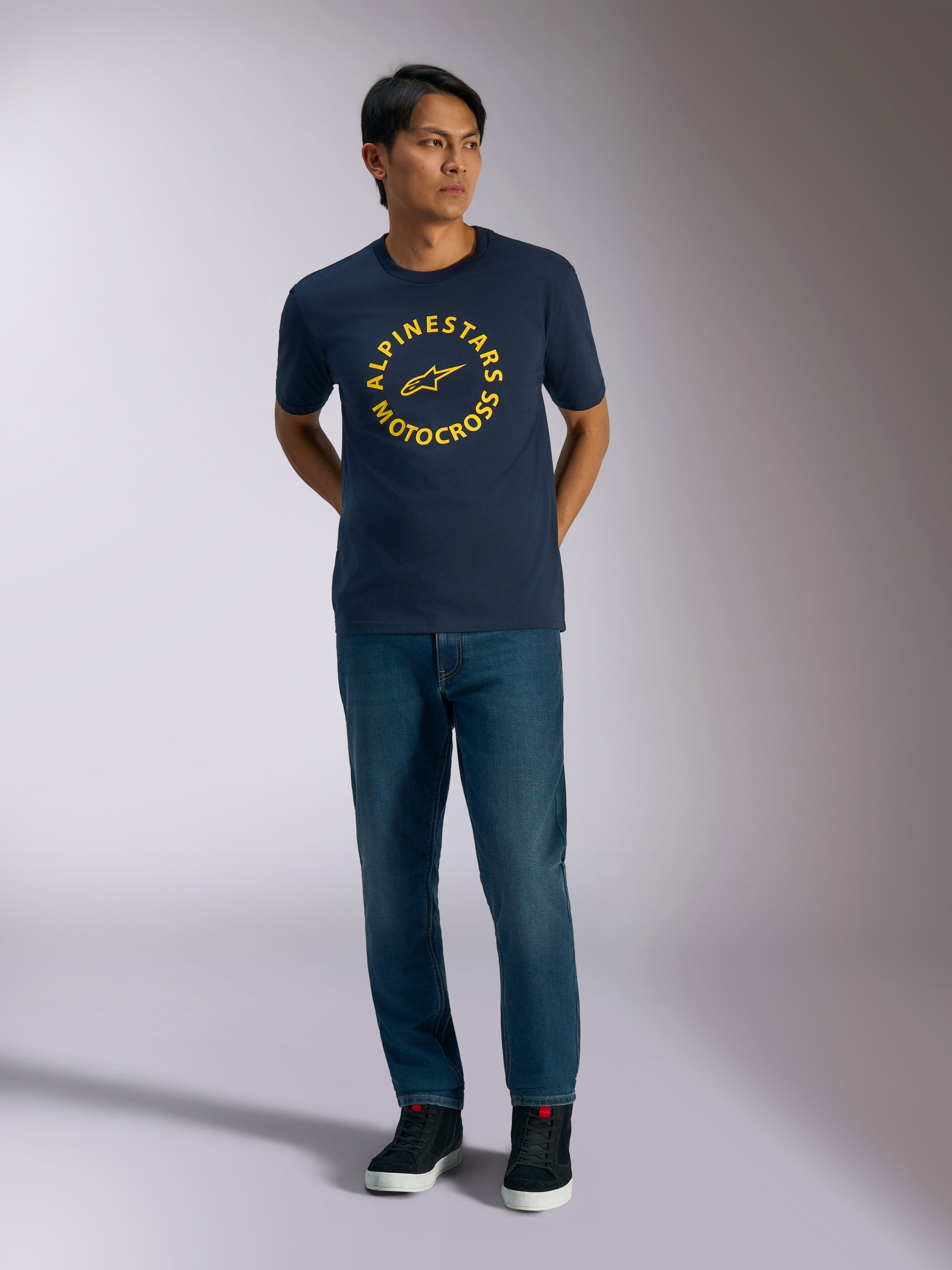 Alpinestars MX CSF Tee, kurzärmeliges T-Shirt, Navyblau, mit einer gelben kreisförmigen Alpinestars Motocross-Grafik, getragen von einem Modell mit blauen Jeans und schwarzen Sneakern, lässige Motorsport-Streetwear