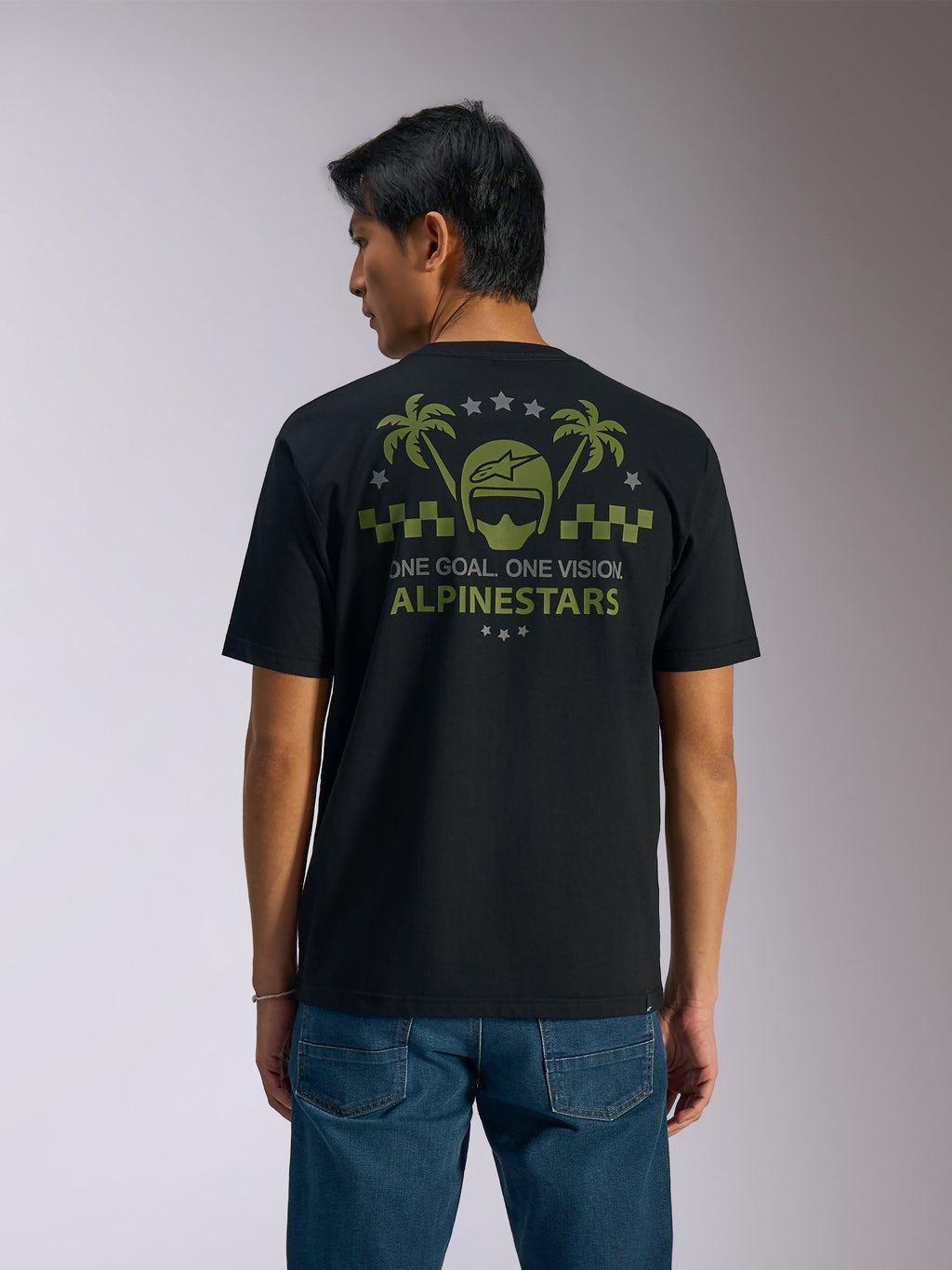 Alpinestars Order CSF Tee, Kurzarm-T-Shirt, Schwarz, Rückansicht, olivgrüne Grafik mit Palmen und Helm-Logo, Text „ONE GOAL. ONE VISION. ALPINESTARS“, kombiniert mit blauen Jeans, lässige Motorsport-Streetwear
