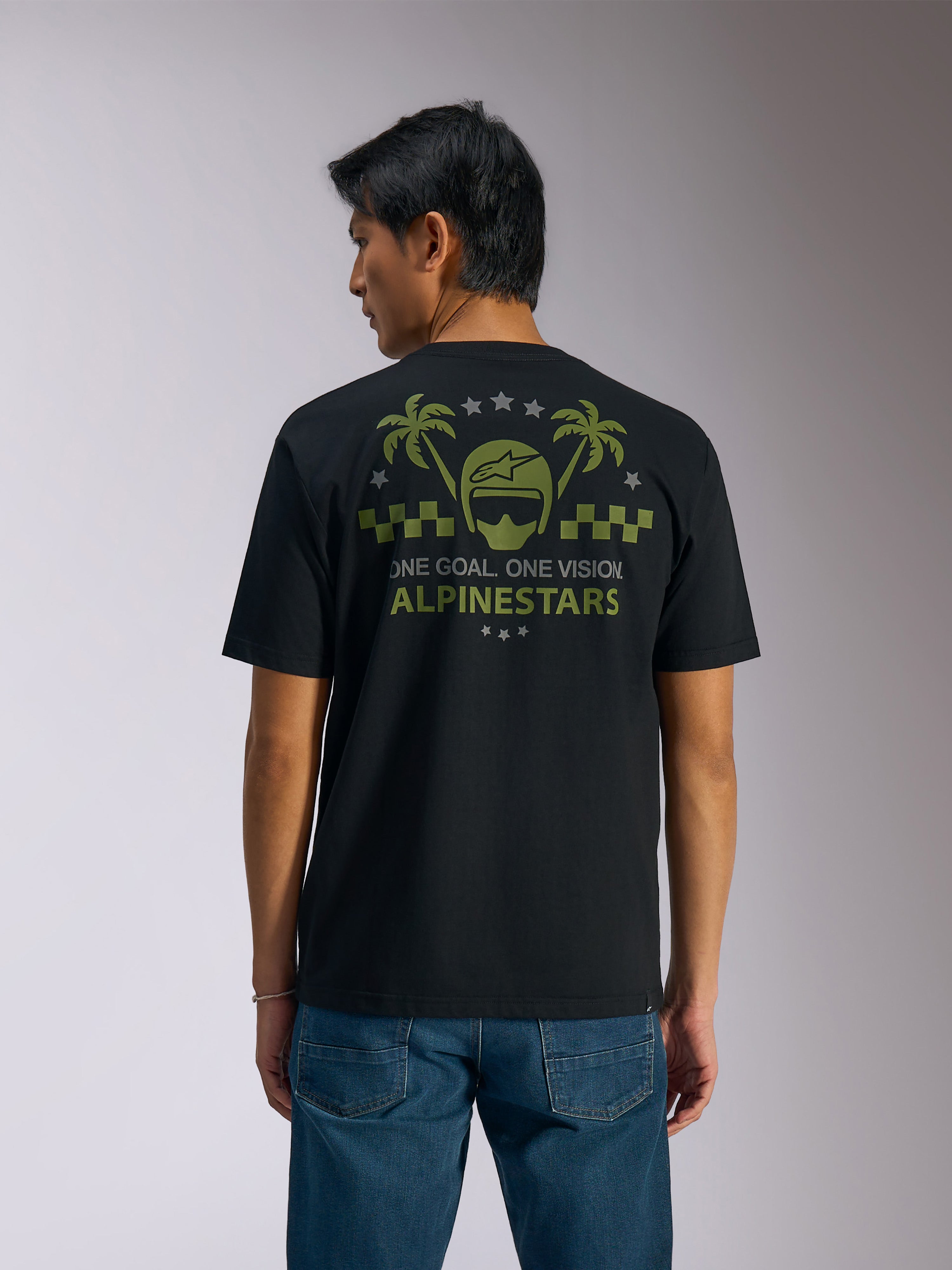 Alpinestars Order CSF Tee, Kurzarm-T-Shirt, Schwarz, Rückansicht, olivgrüne Grafik mit Palmen und Helm-Logo, Text „ONE GOAL. ONE VISION. ALPINESTARS“, kombiniert mit blauen Jeans, lässige Motorsport-Streetwear