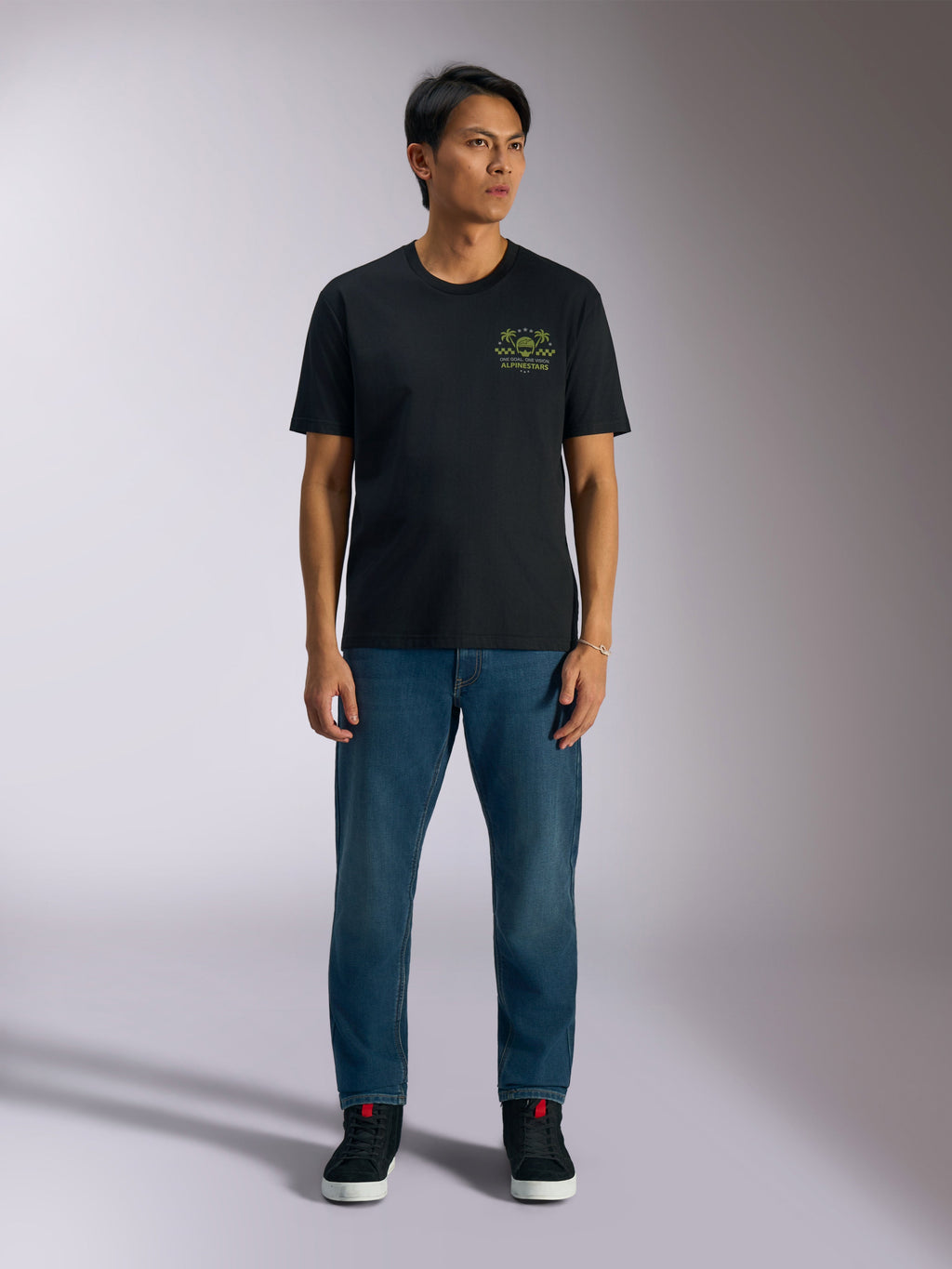 Alpinestars Order CSF T-Shirt, Kurzarm-T-Shirt, Schwarz, limettengrüne Grafik mit Helm und Palmen auf der Brust, getragen mit blauen Jeans und schwarzen Sneakern, legere Motorsport-Streetwear