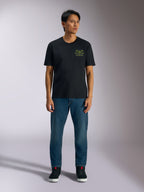 Alpinestars Order CSF T-Shirt, Kurzarm-T-Shirt, Schwarz, limettengrüne Grafik mit Helm und Palmen auf der Brust, getragen mit blauen Jeans und schwarzen Sneakern, legere Motorsport-Streetwear