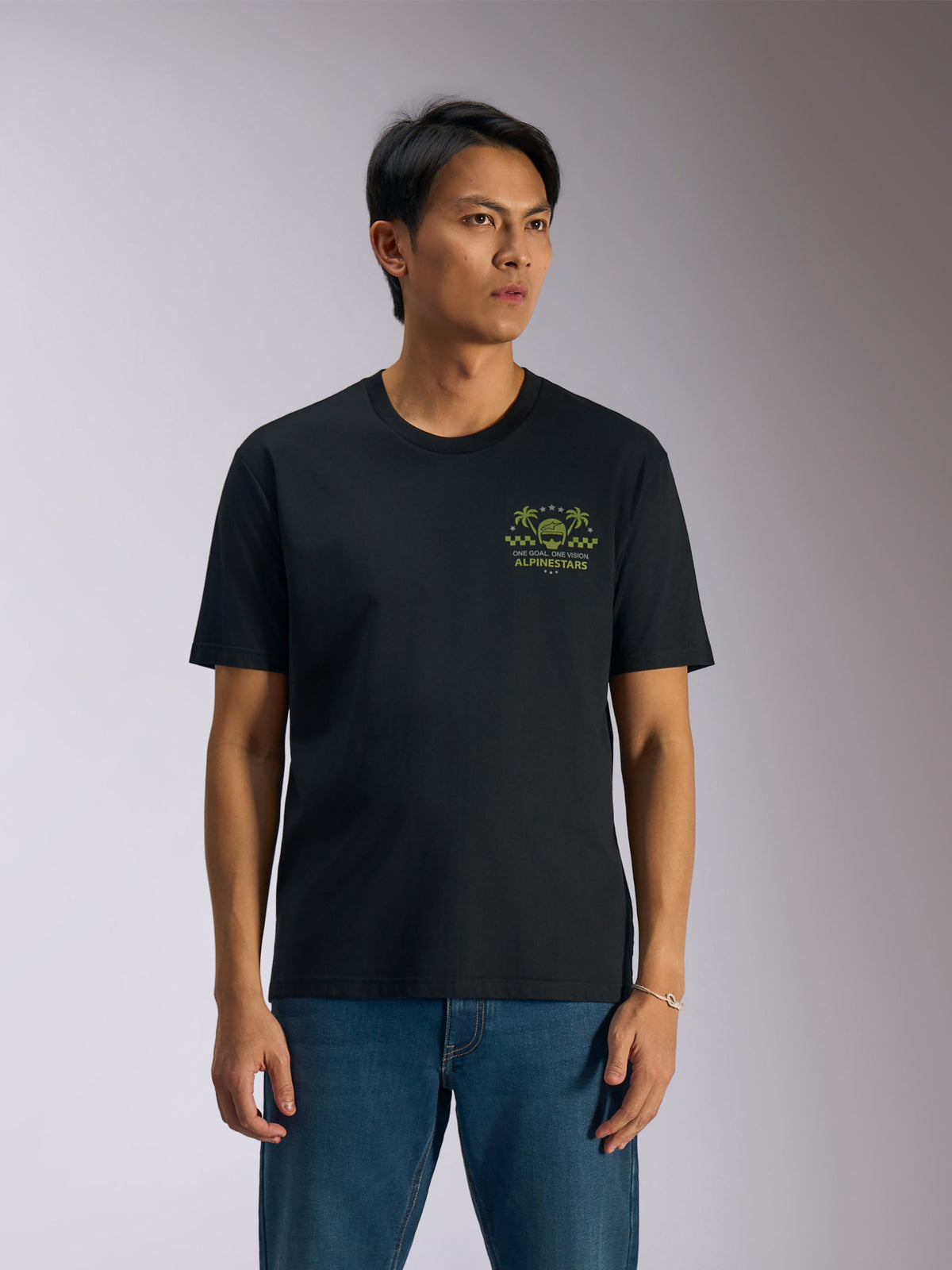 Alpinestars Order CSF Tee, Kurzarm-T-Shirt, Schwarz, grüne Grafik mit Helm und Palmen auf der Brust, kombiniert mit blauen Jeans, lässige Motorsport-Streetwear