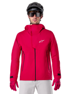 Alpinestars A-Dura Elite Wasserdichte Jacke, Mountainbike-Regenjacke, Rot Fluo, hoher Kragen mit weißem Alpinestars-Logo, schwarze Reißverschluss-Details, getragen mit passenden Handschuhen und schwarzem Fahrradhelm, technische wasserdichte Fahrradausrüstung