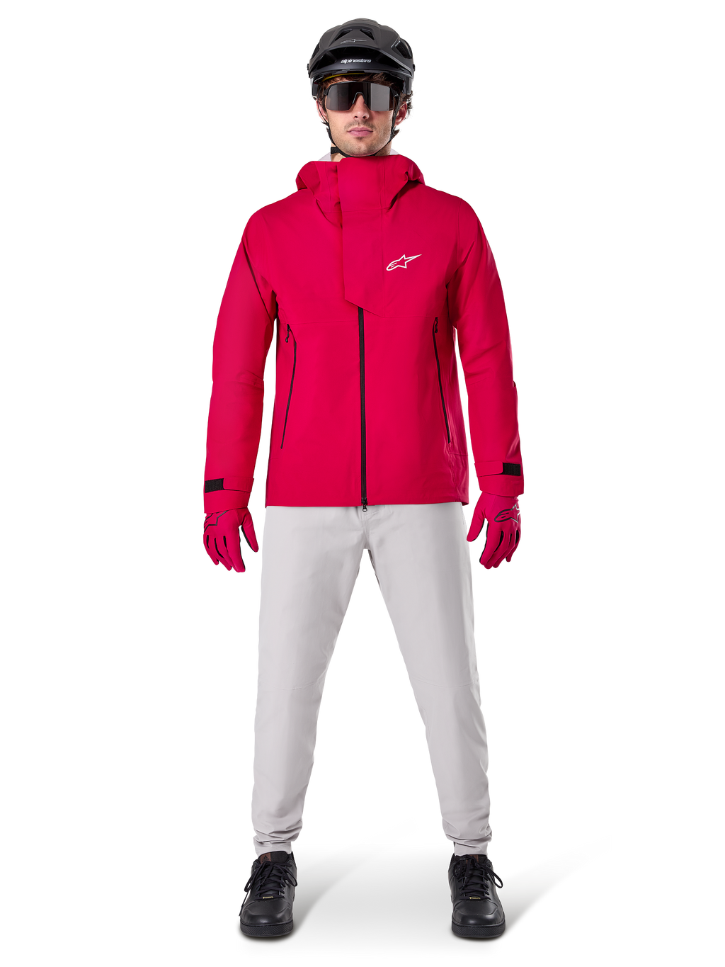Alpinestars A-Dura Elite Wasserdichte Jacke, Red Fluo, technische Mountainbike-Jacke getragen mit einem schwarzen MTB-Helm, Sonnenbrille, passenden roten Handschuhen und hellgrauer Hose, Ganzkörperansicht einer Allwetter-Fahrradausrüstung