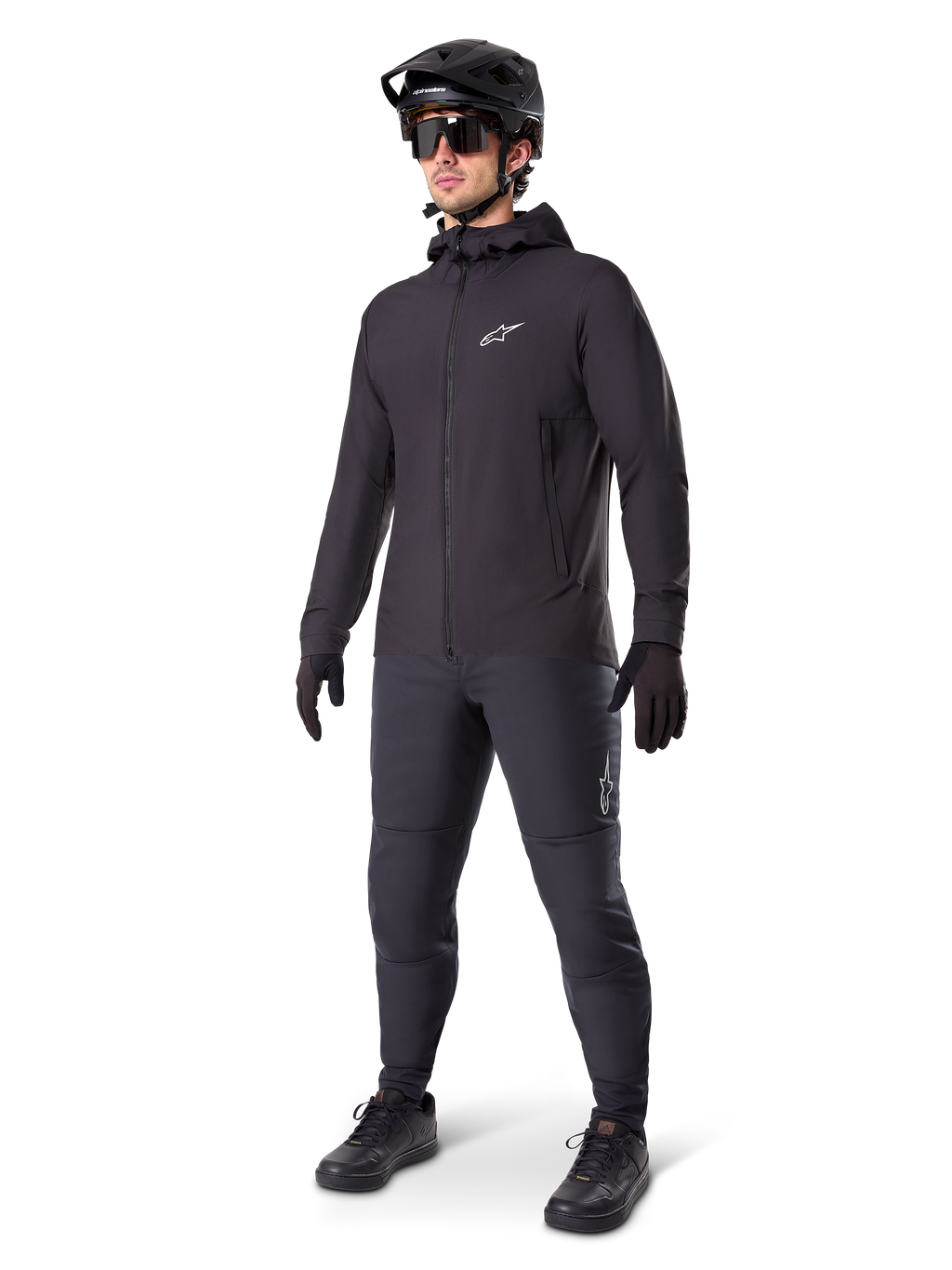 Alpinestars A-Dura Thermal Jacket in Black, worn by a male rider with complete mountain bike gear including a black helmet, sunglasses, and riding pants, lightweight insulated hooded jacket for cold-weather cycling performance.