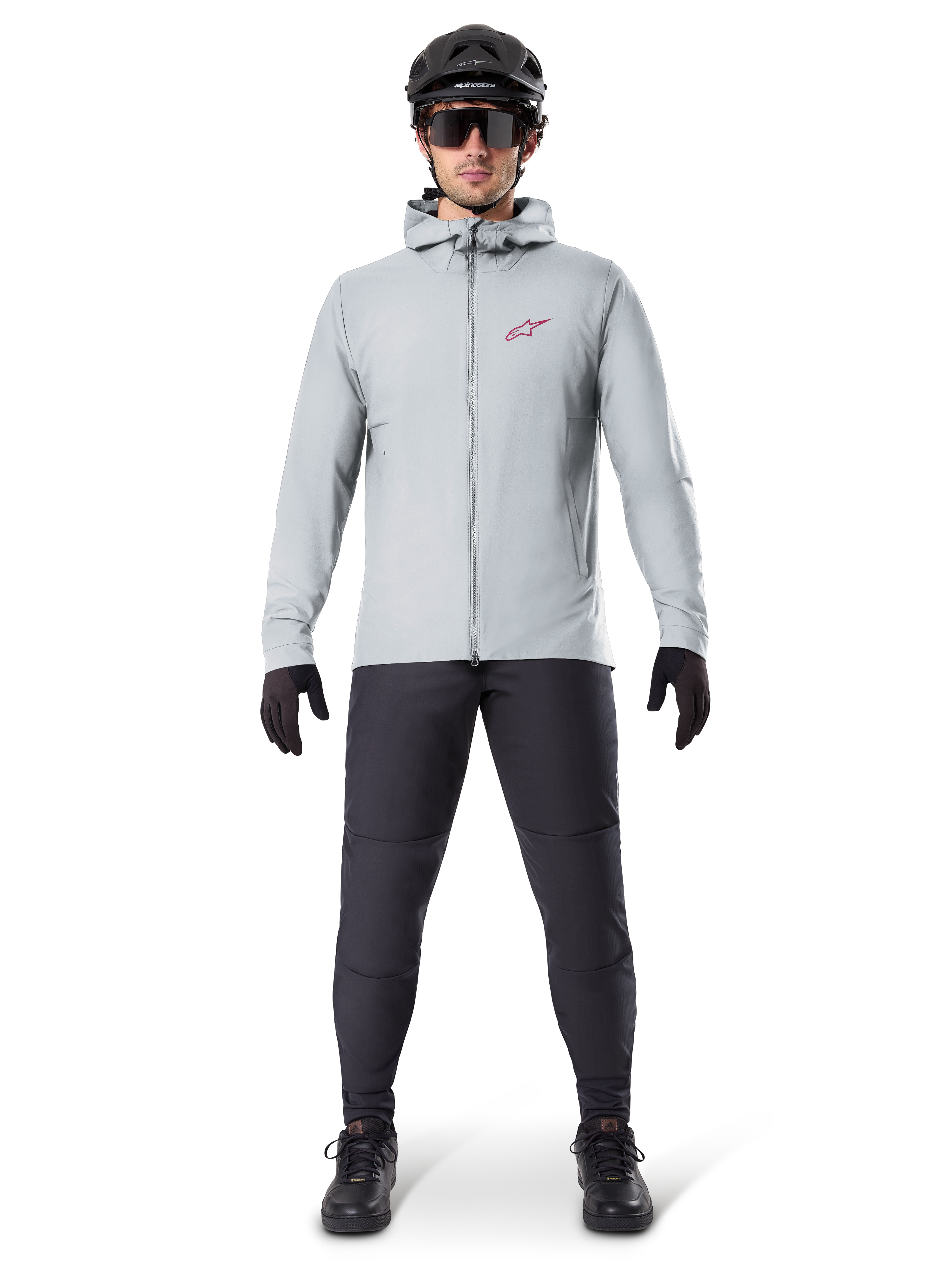 Alpinestars A-Dura Thermojacke, Titanium-Grau, Fahrradjacke getragen mit schwarzer Mountainbike-Hose, Handschuhen und Helm, mit einem kleinen roten Stern-Logo auf der Brust und einem durchgehenden Frontreißverschluss, leichte isolierte Ausrüstung für Offroad-Einsätze.