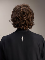 Alpinestars A-Aria Windbreaker Jacke, Schwarz, Nahaufnahme der Rückenansicht von Schultern und Kragen, mit einem kleinen weißen Logo in der Mitte des Rückens, getragen von einem Model mit welligem braunem Haar, minimalistische Performance-Radbekleidung