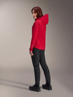 Alpinestars Stella A-Dura Elite Wasserdichte Damenjacke in Red Fluo, kombiniert mit schwarzer technischer Radhose und schwarzen Schuhen, Dreiviertel-Rückansicht mit verstellbarer Kapuze und verlängertem Rückensaum, Performance-Mountainbike-Bekleidung.