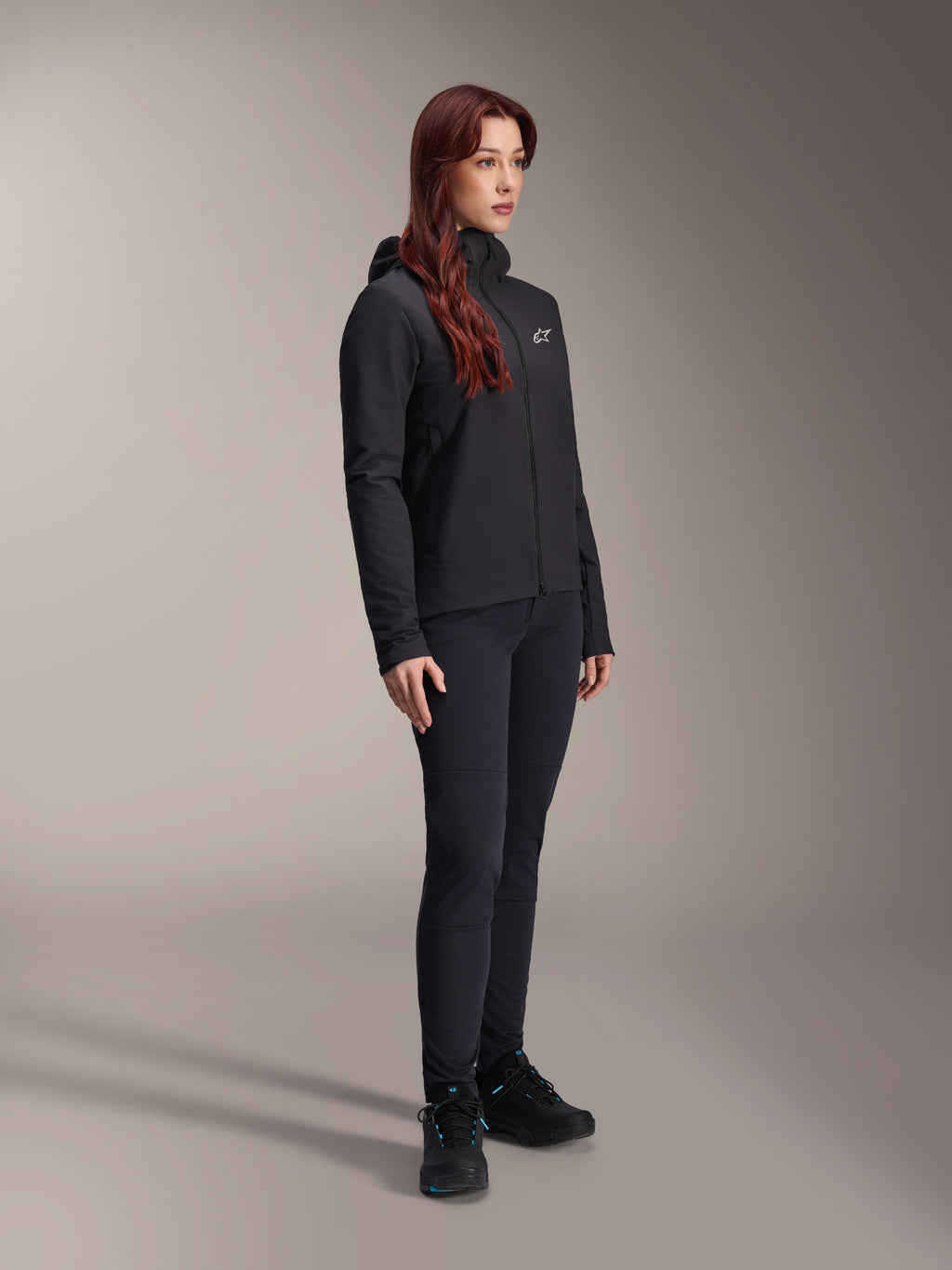Alpinestars Stella A-Dura Thermal Jacke, schwarze, leichte, isolierte Damenjacke mit Kapuze, kombiniert mit schwarzer Hose und schwarzen Schuhen, professionelles Radsport- und Mountainbike-Outfit für kalte Bedingungen